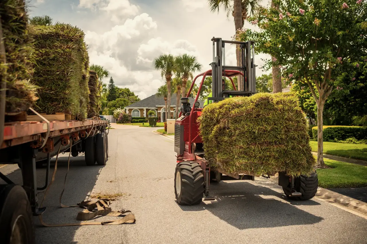 A forklift unloading a pallet of fresh-cut sod from a Grass DFW flatbed on a residential street