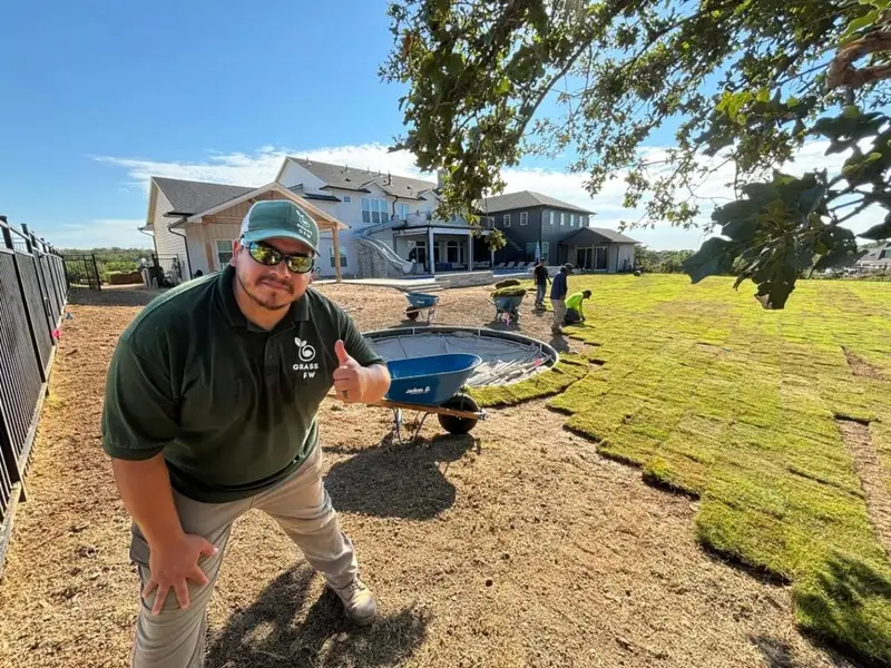 A Grass DFW crew member giving a thumbs up on a yard where the new sod is going down