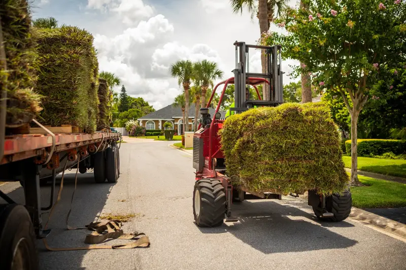 A forklift unloading pallets of sod from a Grass DFW truck
